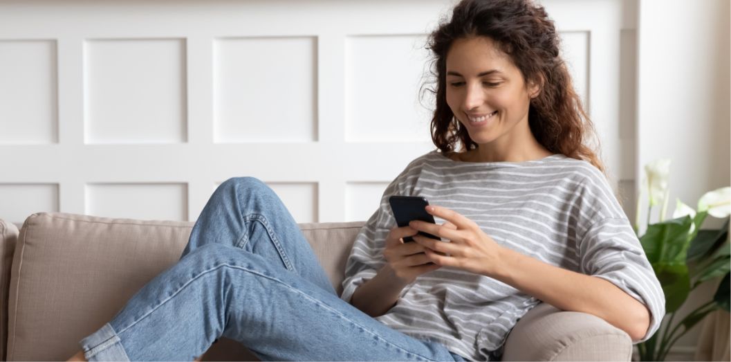 Young Beautiful Women Sitting On The Sofa And Scrolling Down On The Phone